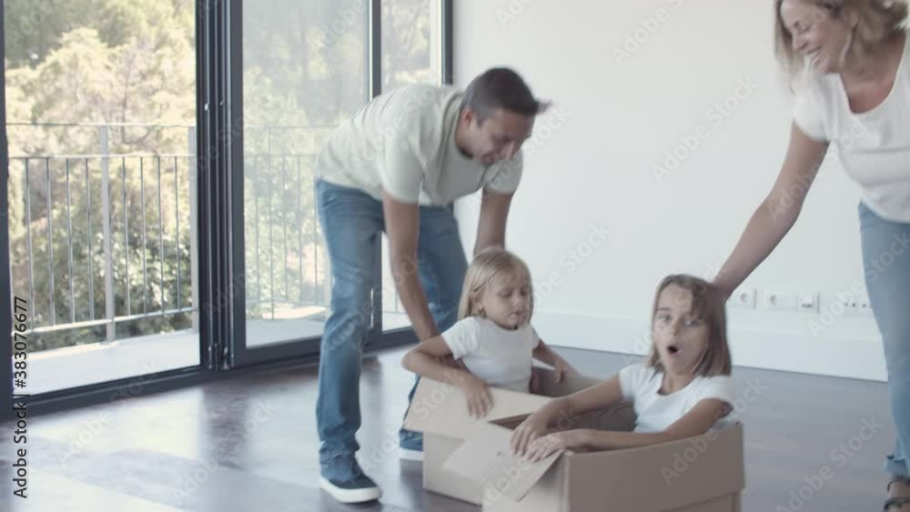 Happy family having fun while moving into new apartment. Parents dragging boxes with daughters inside. Dolly shot. New home concept Happy family having fun while moving into new apartment. Parents dragging boxes with daughters inside. Dolly shot. New home concept