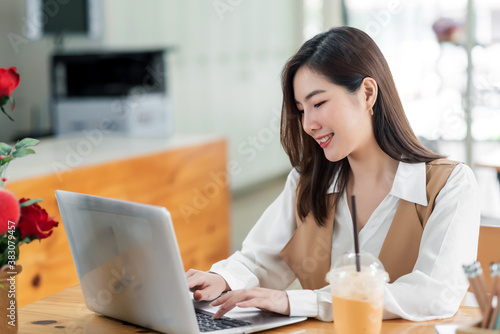 Beautiful young asian woman sitting at coffee shop using laptop. Happy young businesswoman sitting at table in cafe with tab top computer.