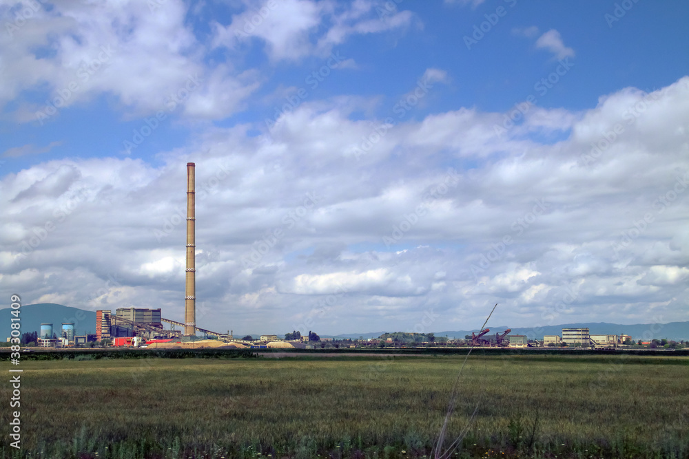Instalaciones industriales próximas a la ciudad de Brasov, Rumanía. Una gran chimenea industrial destaca del resto de instalaciones contra el cielo azul con nubes.