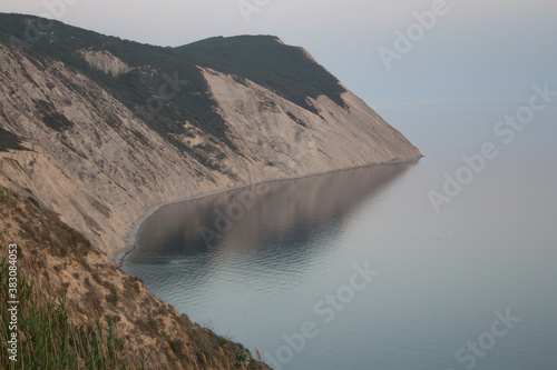  A bay with a beautiful sheer cliff at sunset with blue sea water. Rocks by the ocean, rocky ledge, cliff.