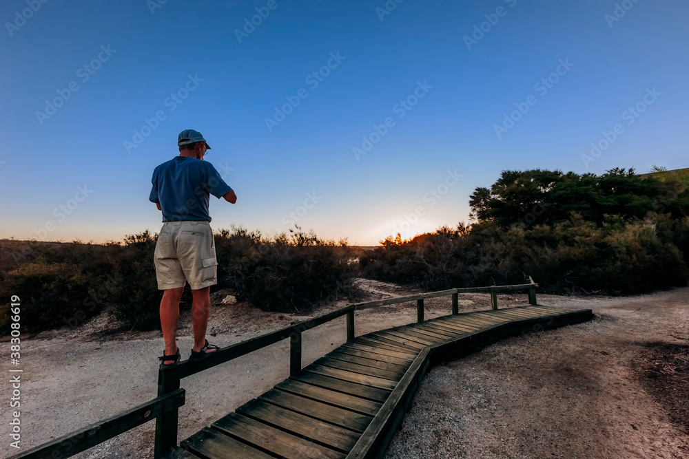 Mature man standing on railing and photographing sunset Mature man standing on railing and photographing sunset