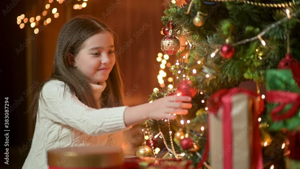 Happy little girl decorating christmas tree with balls. Lots of gift boxes under the tree. children decorating a Christmas tree.