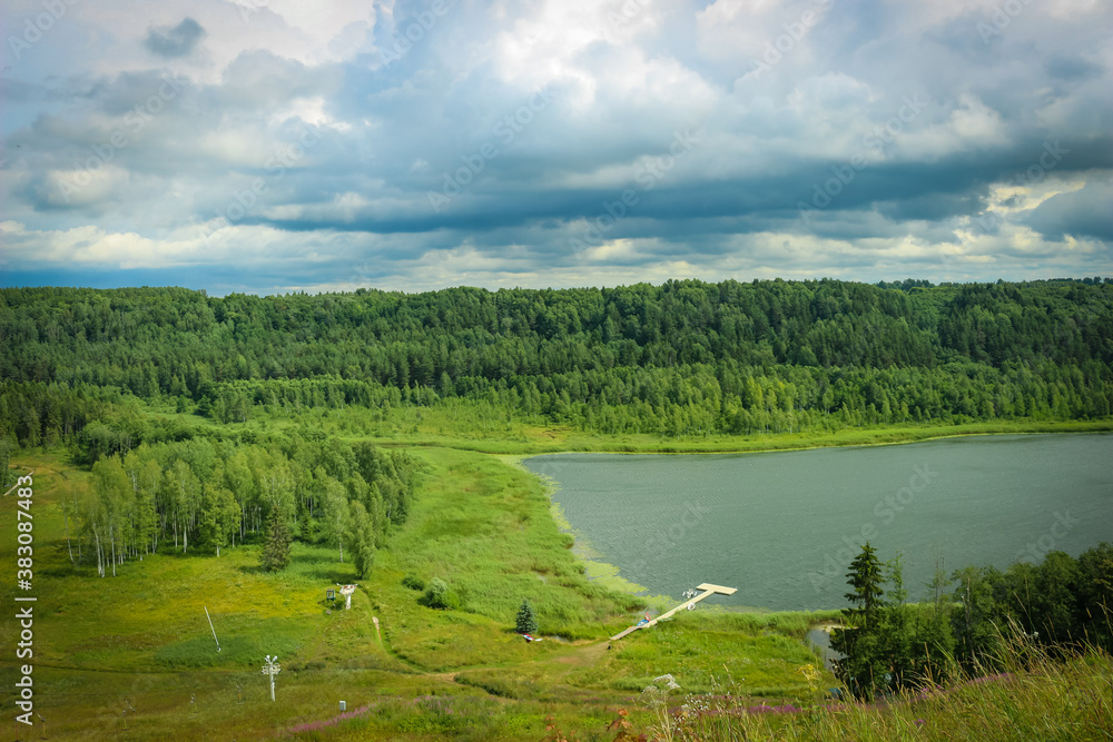Fototapeta premium River landscape with forest hill slopes and cloudy sky at background.