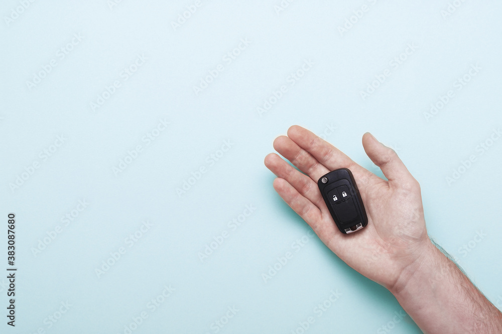 Male hand holds car keys on pastel blue background. Concept car, car rental, gift, driving lessons, driving license. Flat lay, top view Male hand holds car keys on pastel blue background. Concept car, car rental, gift, driving lessons, driving license. Flat lay, top view