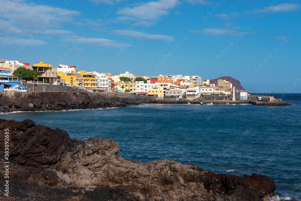 Black volcanic rocks framing the traditional Spanish village  with colorful buildings, a small harbor and the Atlantic ocean in front, in Los Abrigos, Tenerife, Canary Islands, Spain