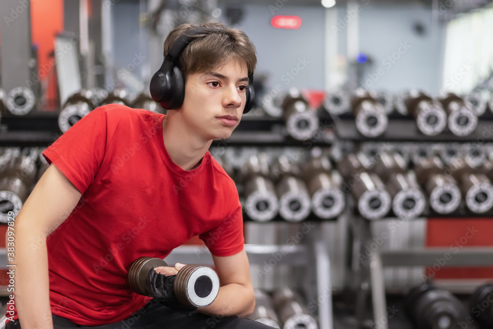 young man in sportswear and headphones works out with dumbbells in the gym young man in sportswear and headphones works out with dumbbells in the gym