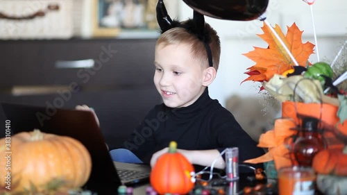 funny kid boy in witch costume for Halloween using a digital tablet laptop notebook. Online call friends or parents