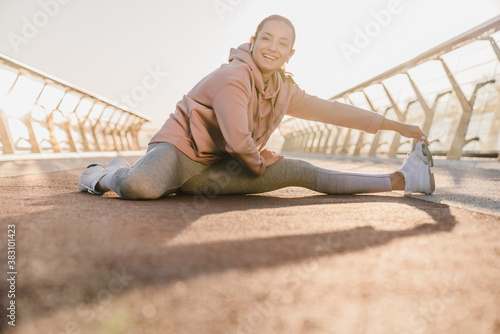 Portrait of smiling fit and sporty young woman doing stretching in city on bridge.