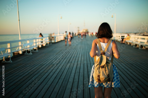 Young female tourist with vintage backpack walking on the wooden pier in golden hour