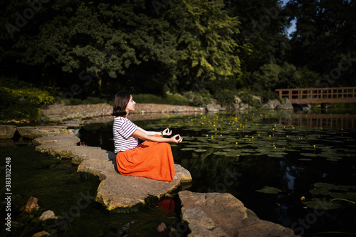 Young woman sitting on the pound shore in lotus pose