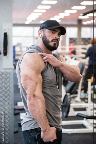 strong young bearded male showing big triceps muscle during posing in sport gym after hard workout training
