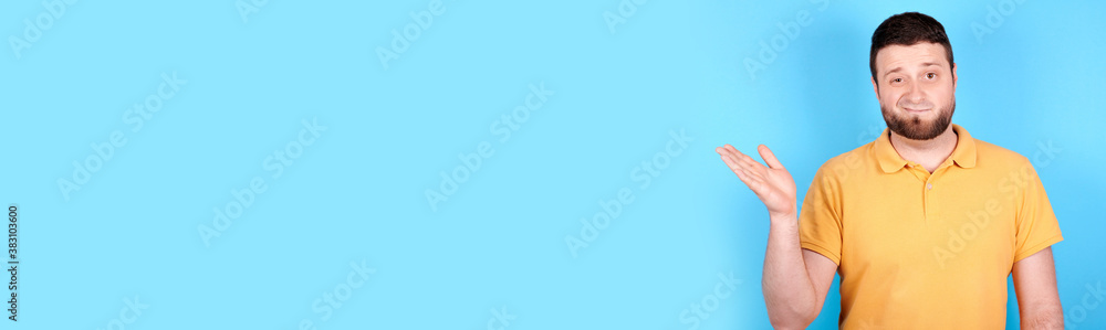 Brunette man spreads his arm to the side, disappointment emotion. Isolated on blue background, copy space template, banner. Brunette man spreads his arm to the side, disappointment emotion. Isolated on blue background, copy space template, banner.