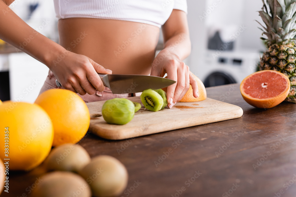 Cropped view of young woman cutting kiwi near fresh fruits on table Cropped view of young woman cutting kiwi near fresh fruits on table