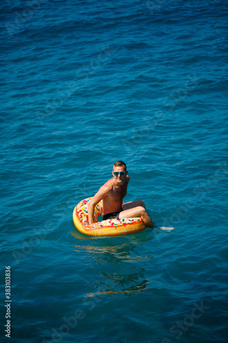 A young man floats on an inflatable air ring circle in the sea with blue water. Festive holiday on a happy sunny day. Vacation concept, top view. © Дмитрий Ткачук