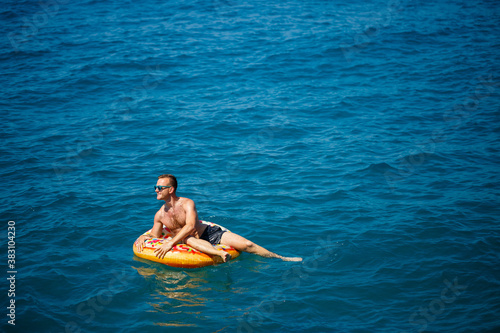 a man lies on a large inflatable rubber circle and floats on the blue sea on a bright sunny summer day © Дмитрий Ткачук