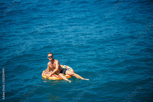 a man lies on a large inflatable rubber circle and floats on the blue sea on a bright sunny summer day