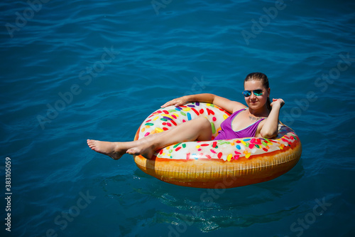 A young beautiful girl in a bright swimsuit lies on a large inflatable ring and floats on the blue sea on a bright sunny summer day © Дмитрий Ткачук