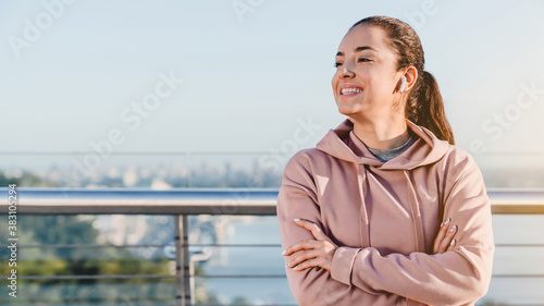 Happy lady jogger is resting after workout standing on the bridge against city landscape © InsideCreativeHouse