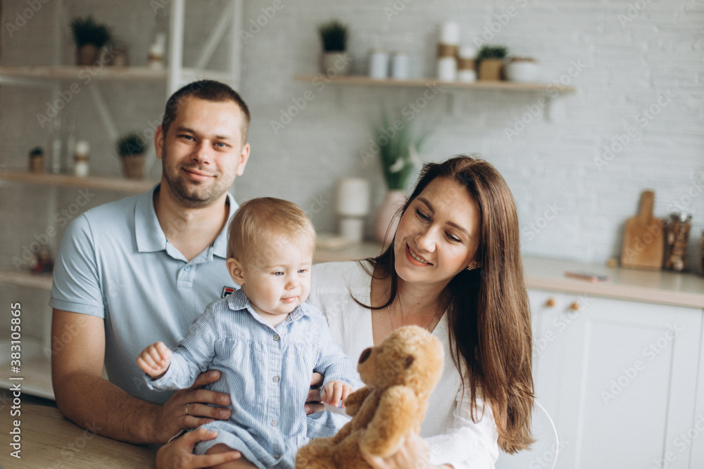 Happy cheerful young family together with infant baby girl in kitchen at home