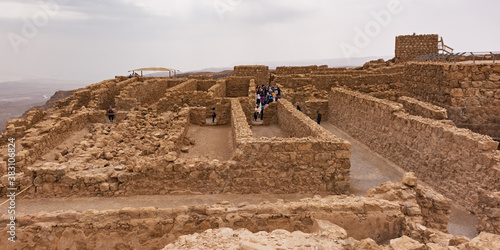 tourists in the storerooms complex on the northwest side of masada  in israel with the guard tower and bathhouse on the right and storm clouds in the background photo