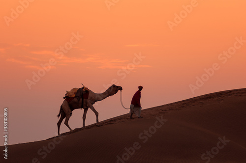 Man and a camel walking across sand dunes in Jaisalmer, Rajasthan, India.