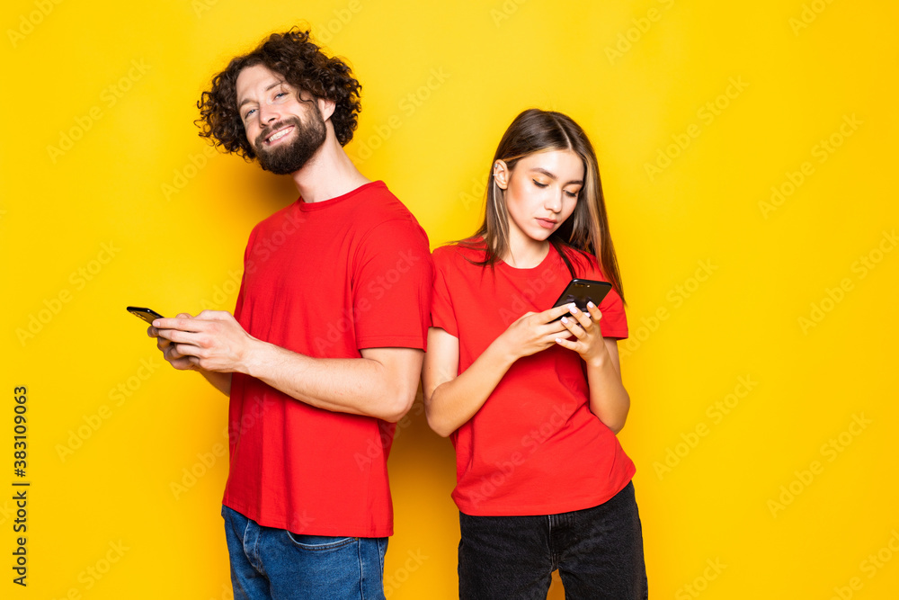 Obraz premium Photo of excited people man and woman holding smartphones in hands isolated over yellow background