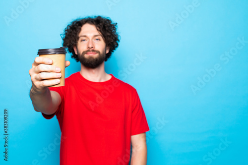 Portrait of a smiling young man pointed cup of coffee isolated on a blue background.