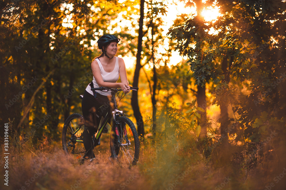 Obraz premium Morning bike ride in the park. A woman in the rays of the rising sun among the trees.