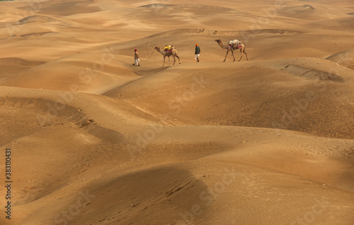 Man with camel walking across sand dunes in Jaisalmer  Rajasthan  India.