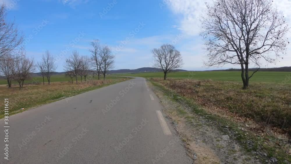 Pov view of biking in the countryside. Healthy and eco transport. Cycling on an asphalt road, around trees and a green meadow. A village in the distance. Blue sky with white clouds. Pov view of biking in the countryside. Healthy and eco transport. Cycling on an asphalt road, around trees and a green meadow. A village in the distance. Blue sky with white clouds.