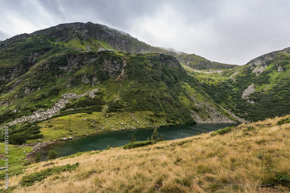 Fototapeta premium green hills with a mountain lake while hiking