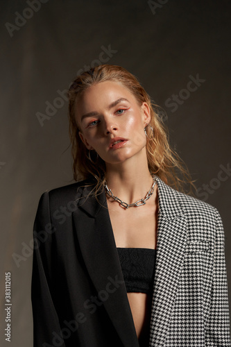 Fashion studio portrait. Elegant woman with make-up and wet blonde hair.Pretty slim female woman in bandeau top and blazer with chain necklace posing against textile background
