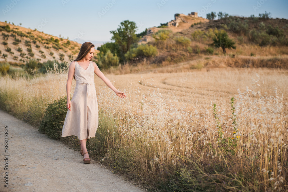 a beautiful woman walks relaxed touching the wheat field. Long-haired blonde girl in white dress walking on a summer afternoon