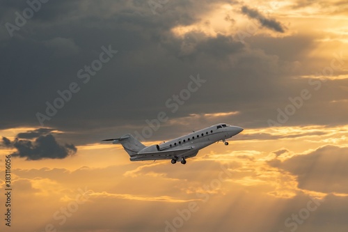 Side view of white business jet with turbofan engines. Attractive orange cloudy sunset sky over the airport. Modern technology in fast transportation, business travel and tourism, aviation.