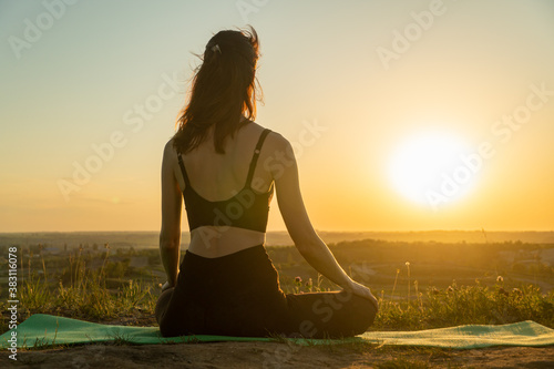 Young woman meditating in a yoga lotus pose on nature at sunset. Concept of healthy lifestyle and relaxation