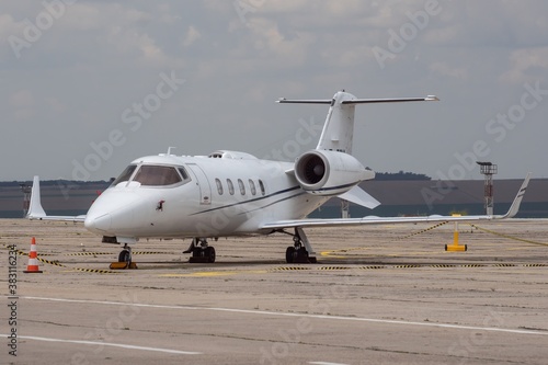 Side view of white business airplane with jet engines. Attractive cloudy sky over the airport. Modern technology in fast transportation, business travel and tourism, aviation.