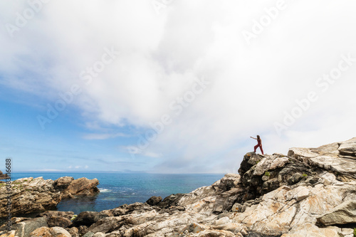 general shot of the Galician coast with a woman perched on some rocks observing the horizon