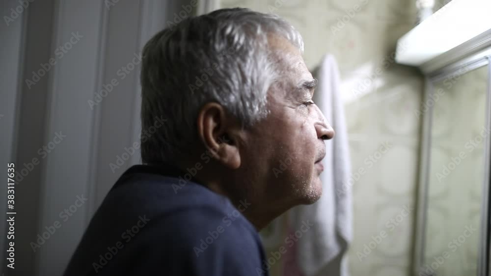 Contemplative older man suffering alone in front of bathroom mirror Contemplative older man suffering alone in front of bathroom mirror