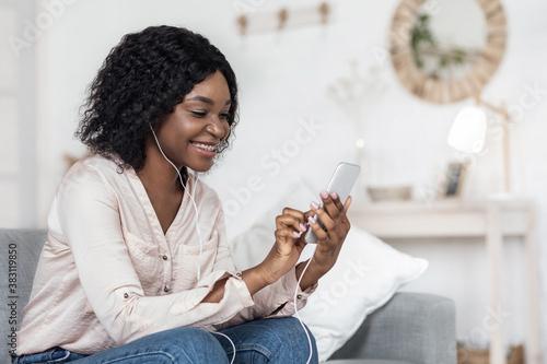 Happy African Woman Browsing Internet On Smartphone And Listening Music At Home