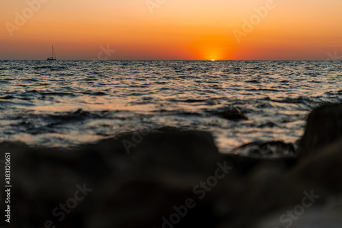 The sun goes into the sea or ocean at sunset  photographed from under the rocks on the shore
