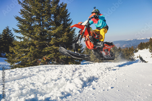 Snowbike rider in mountain valley in beautiful snow powder. Snowdirt bike with splashes and trail. Snowmobile winter sport riding