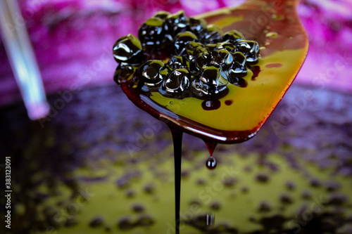 A group of chokeberry berries on a wooden cooking spoon, liquid jam leaks and drips down the spoon into a pot with chokeberry jam.