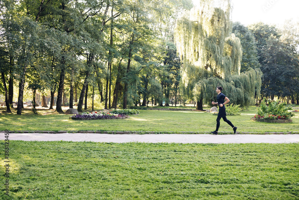 Man in summer sports uniform running in the city park with smartwatch for measuring speed, distance and heart rate. Wireless earphones. Training outside. Man in summer sports uniform running in the city park with smartwatch for measuring speed, distance and heart rate. Wireless earphones. Training outside.