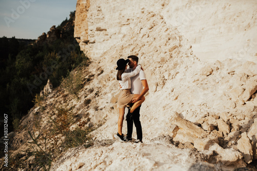 Romantic couple in love standing on the stony mountain. Couple of handsome bearded man in t-shirt and sexy young stylish girl are hugging. Scenic mountain view.