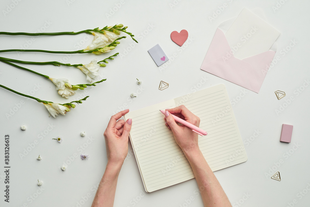 Minimal background composition of female hands writing in planner against while table background with floral decor, copy space Minimal background composition of female hands writing in planner against while table background with floral decor, copy space