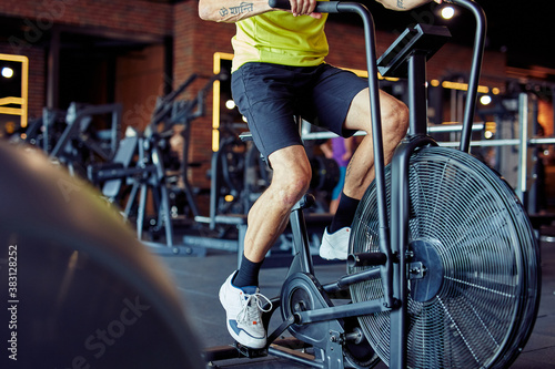 Cropped shot of athletic man in sportswear doing cycling on exercise bikes at gym, cardio workout