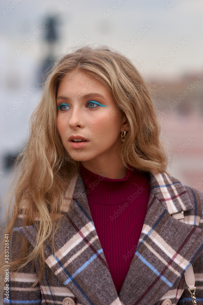 Elegant woman walking city street. Fashion fall autumn look. Pretty caucasian blonde stylish girl wearing blue jeans, wine red pullover and squared wool coat. Female with makeup and wavy blonde hair Elegant woman walking city street. Fashion fall autumn look. Pretty caucasian blonde stylish girl wearing blue jeans, wine red pullover and squared wool coat. Female with makeup and wavy blonde hair
