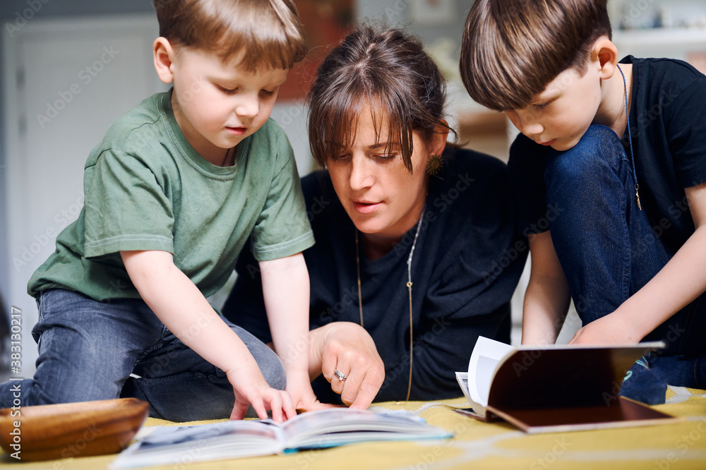 Young caucasian mother spending time at home with sons and reading books on the floor. Happy parent playing with preshool children. Home education concept Young caucasian mother spending time at home with sons and reading books on the floor. Happy parent playing with preshool children. Home education concept