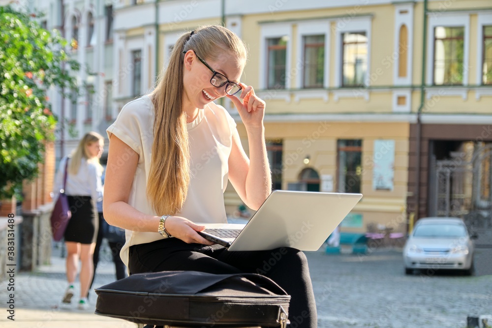 Fototapeta premium Young businesswoman with laptop outdoors, female looking at computer screen