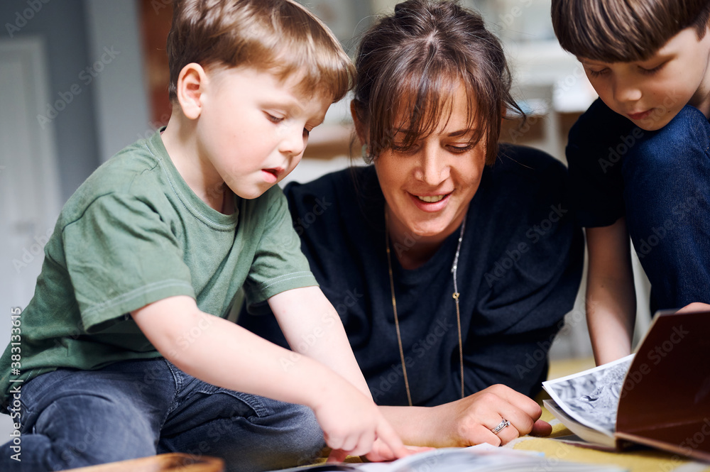Young caucasian mother spending time at home with sons and reading books on the floor. Happy parent playing with preshool children. Home education concept Young caucasian mother spending time at home with sons and reading books on the floor. Happy parent playing with preshool children. Home education concept